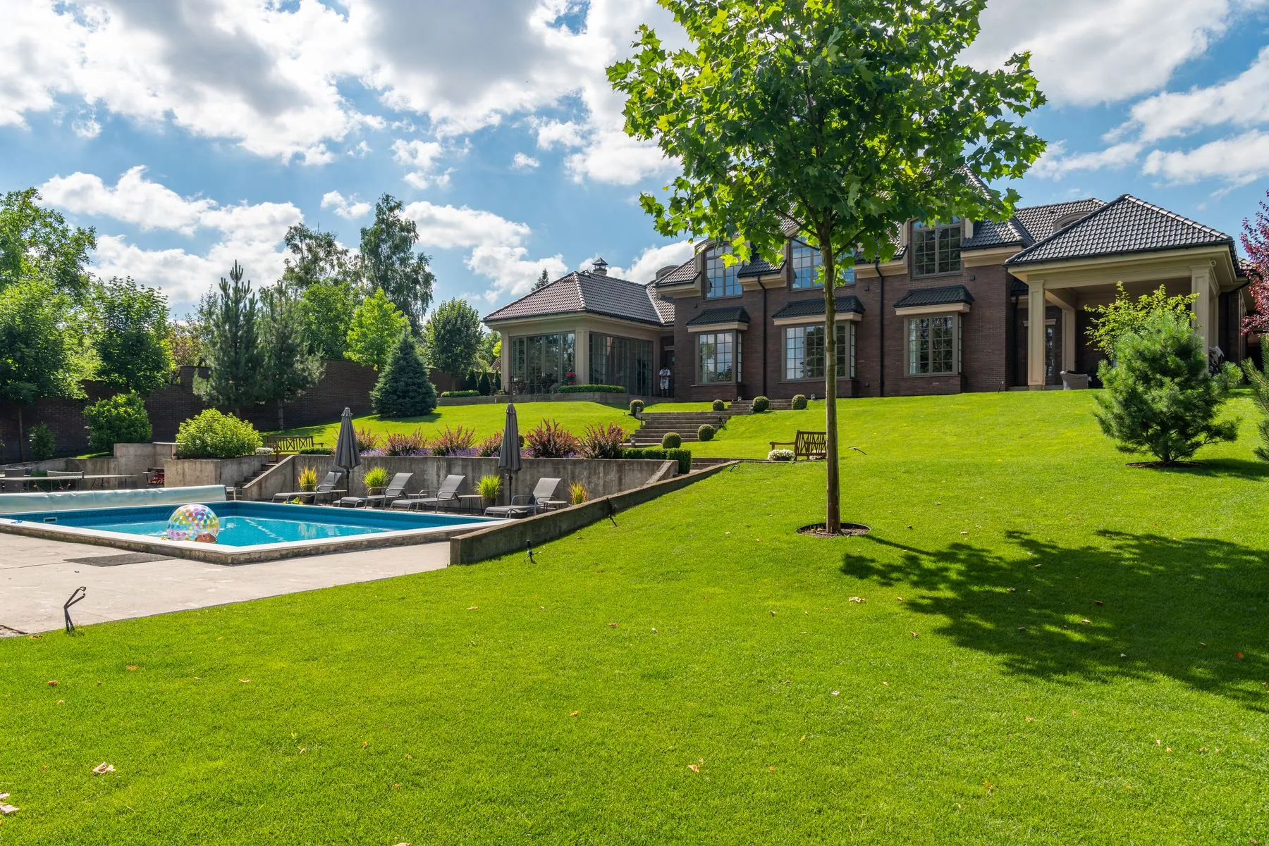 A wide lawn running down to a pool and a country house